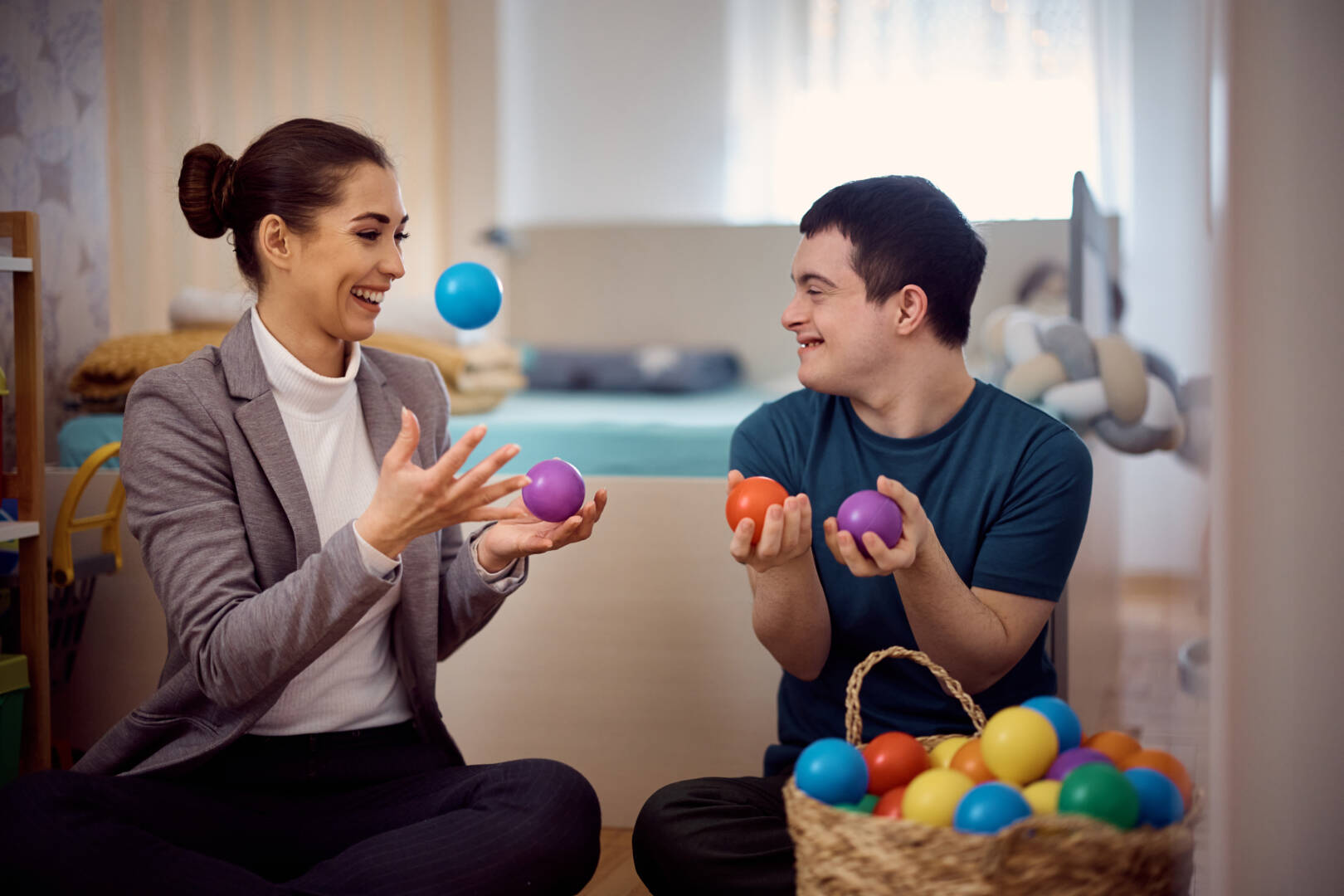 Playful man with down syndrome and his therapist having fun with plastic ball at home.